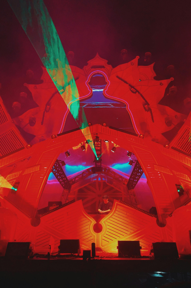 A dramatic stage at a music festival, with vibrant laser lights and neon outlines of a human figure, creating an electrifying atmosphere for a live performance.